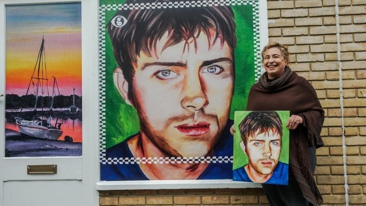 An artist smiling with her painting of Damon Albarn as part of Street Stories